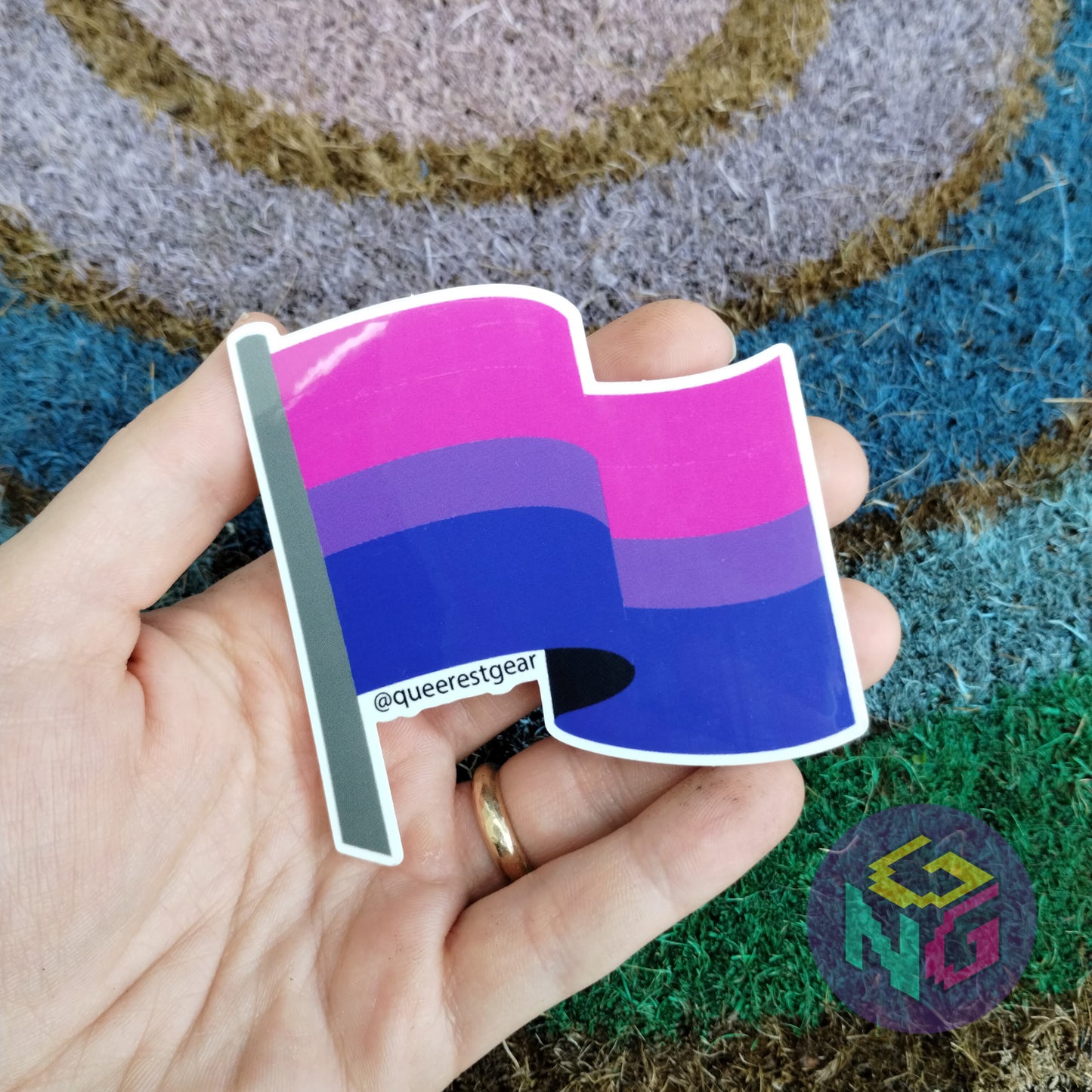 bisexual flag sticker held in hand in front of rainbow welcome mat