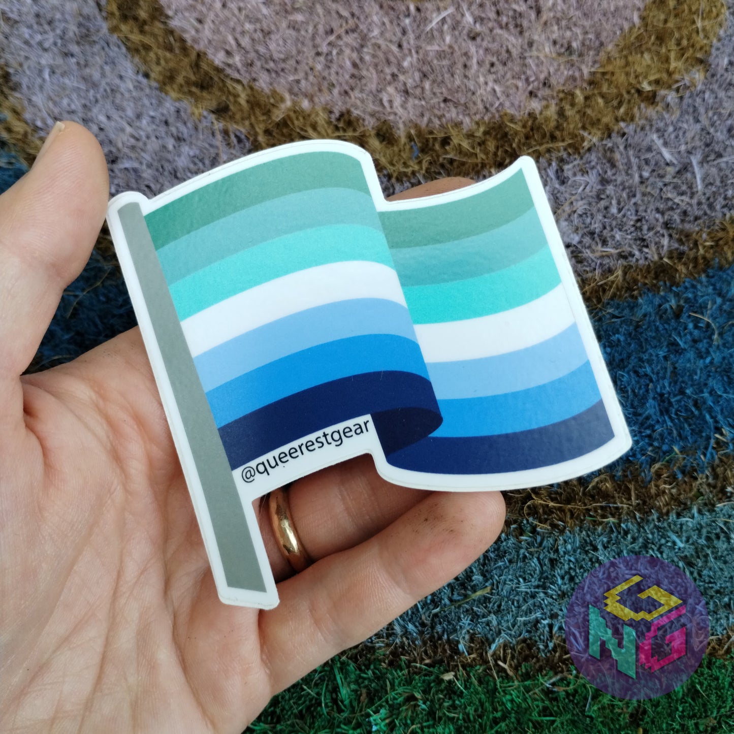 gay mlm flag held in a hand in front of rainbow welcome mat