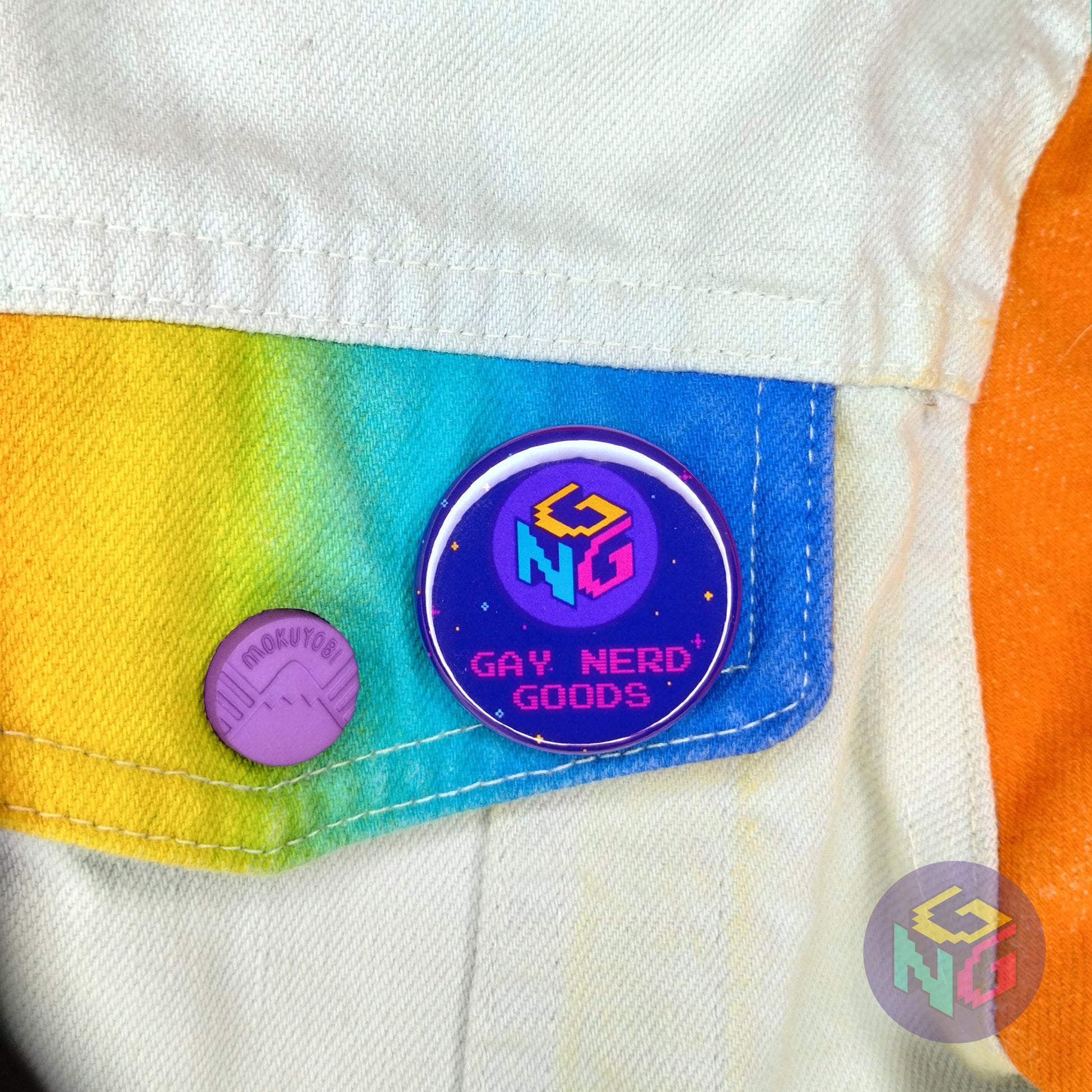 gay nerd goods 1.5" round logo button on the chest pocket of a white denim jacket with rainbow pocket flaps