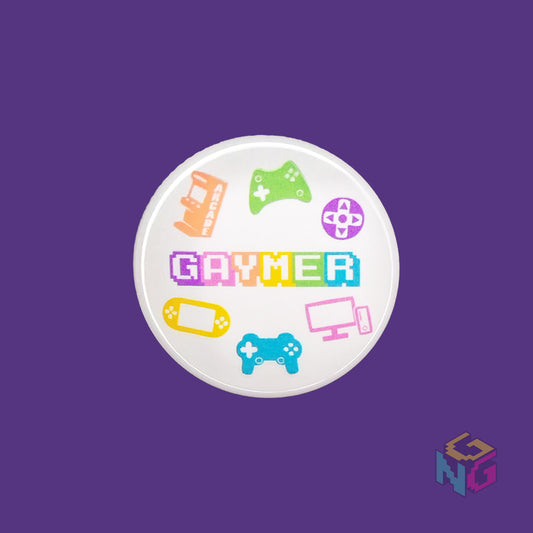 round 1.5" gaymer pinback button flat on purple background. Design features word "gaymer" surrounded by consoles, controllers, and a PC in rainbow colors on a white background