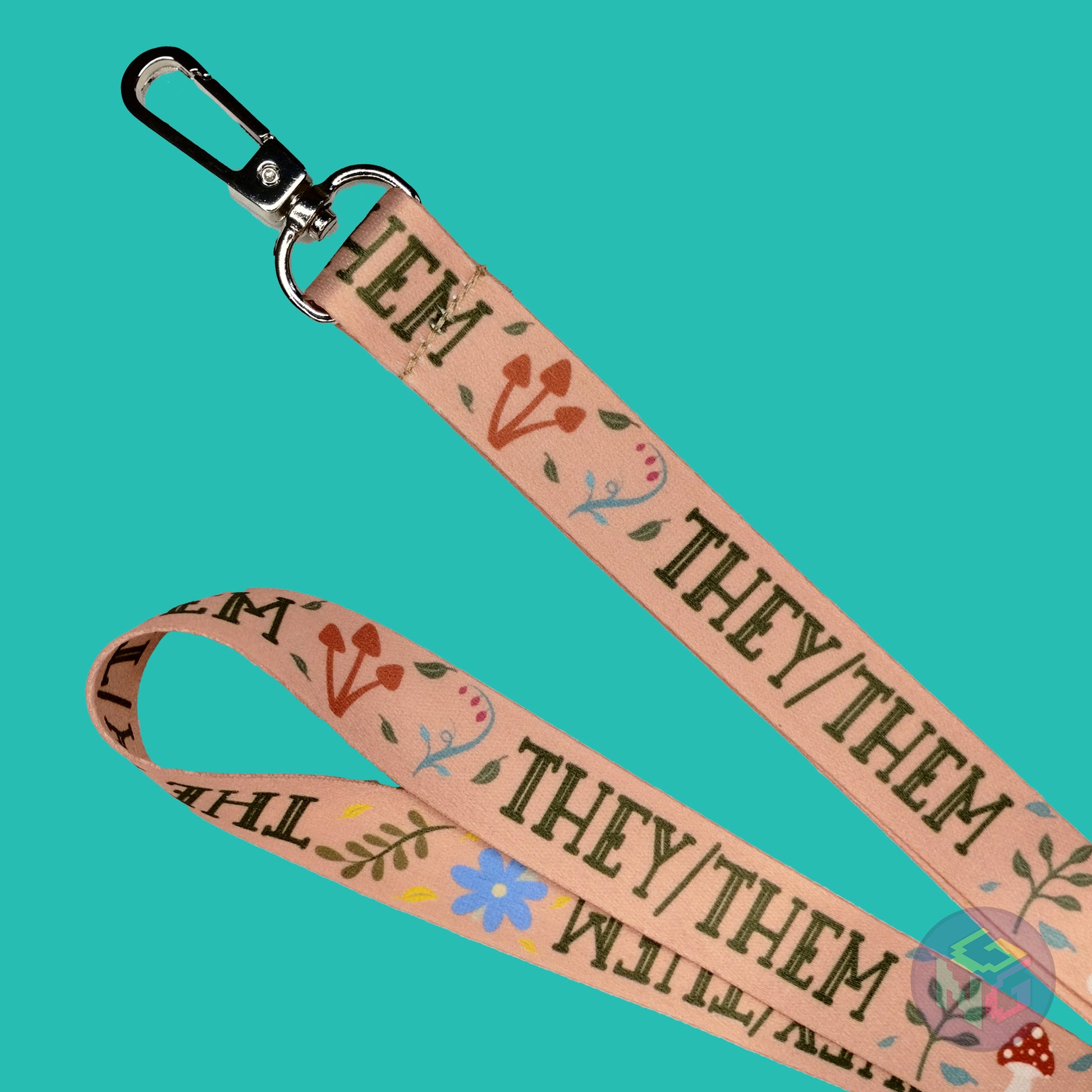 close up detail of the green they them nature lanyard showing the lobster clasp, brown mushrooms, green leaves, and all caps text