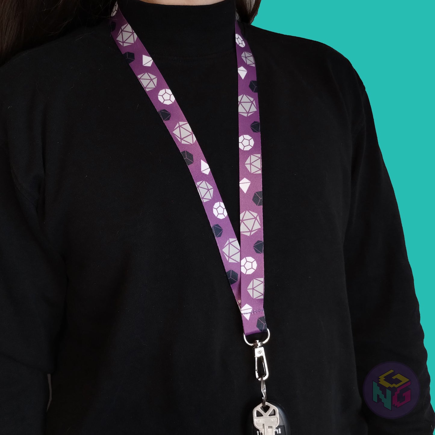 purple asexual pride lanyard being worn by a flat chested person wearing a black turtleneck. The end of the lanyard falls between their sternum and bellybutton and has a key fob clipped to the end