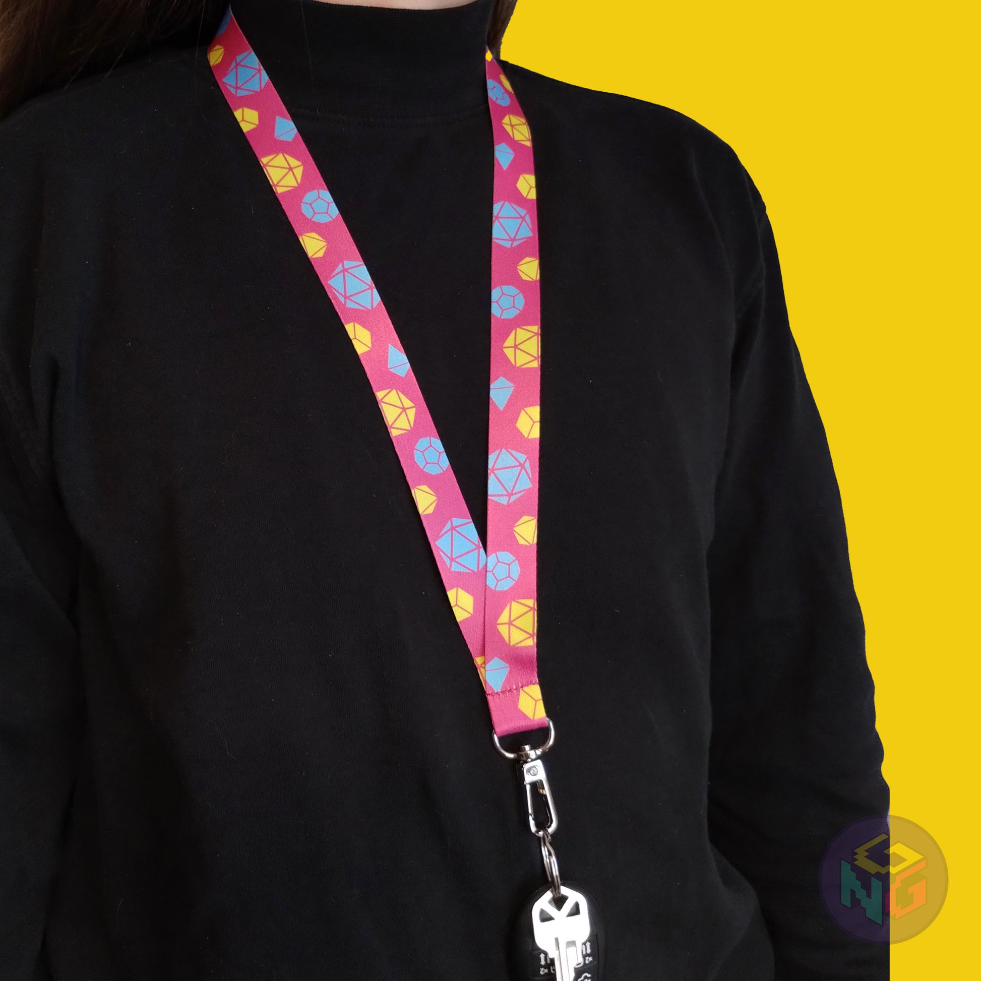 pink pansexual pride lanyard being worn by a flat chested person wearing a black turtleneck. The end of the lanyard falls between their sternum and bellybutton and has a key fob clipped to the end