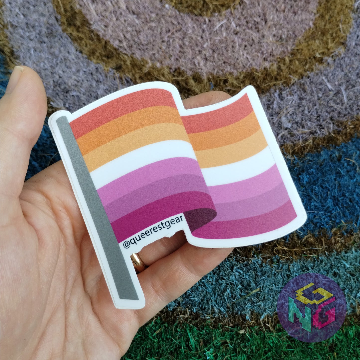 vinyl lesbian flag sticker held in a hand in front of rainbow welcome mat