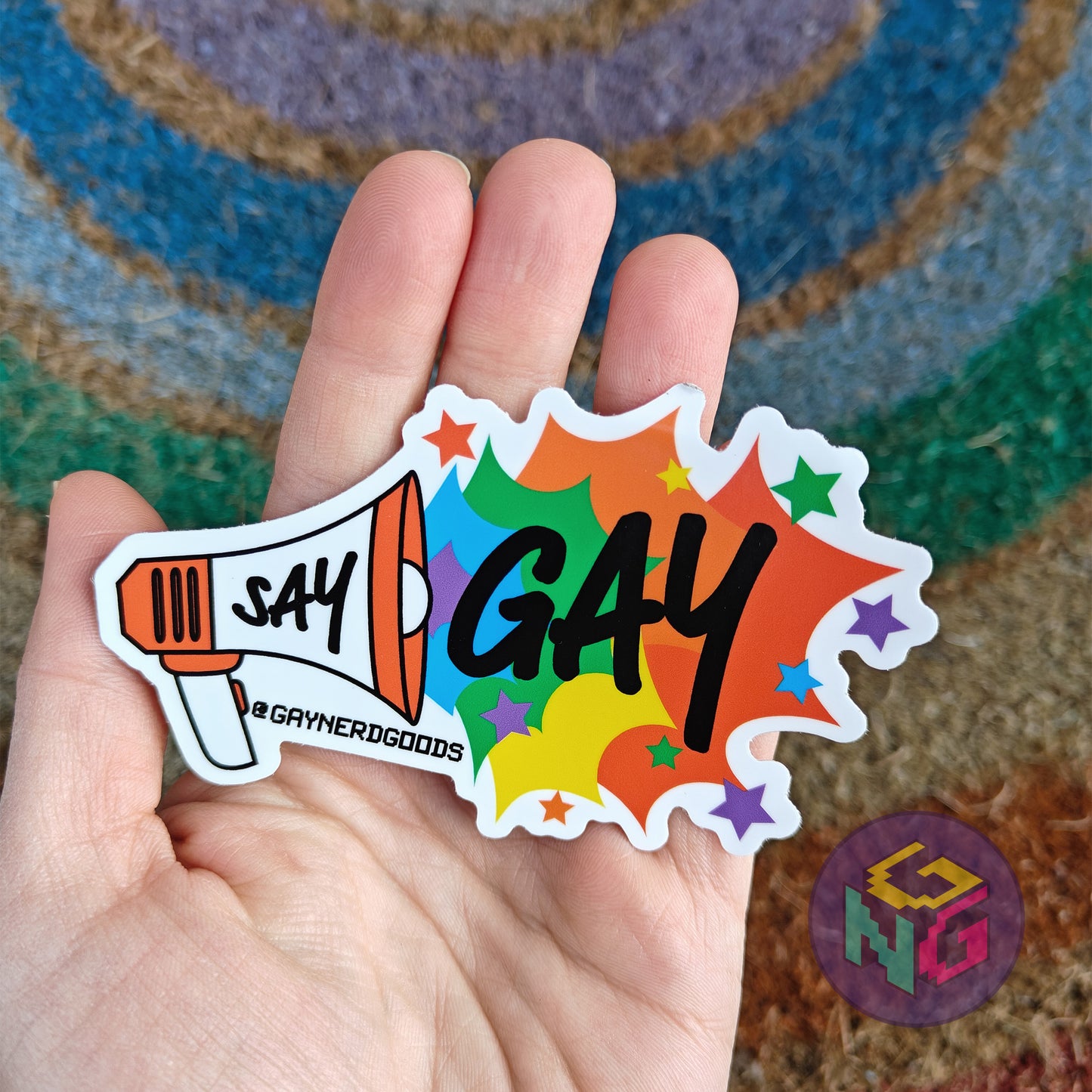 say gay rainbow megaphone waterproof sticker held in front of a neutral rainbow background