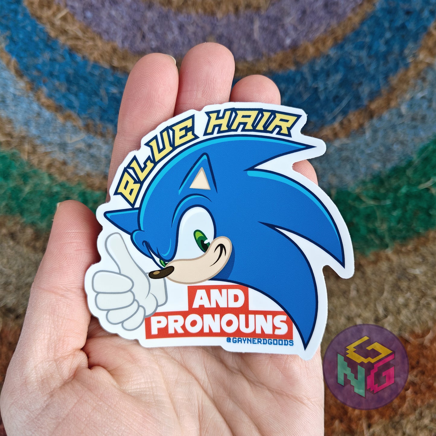 sonic blue hair and pronouns waterproof sticker held in front of a neutral rainbow background
