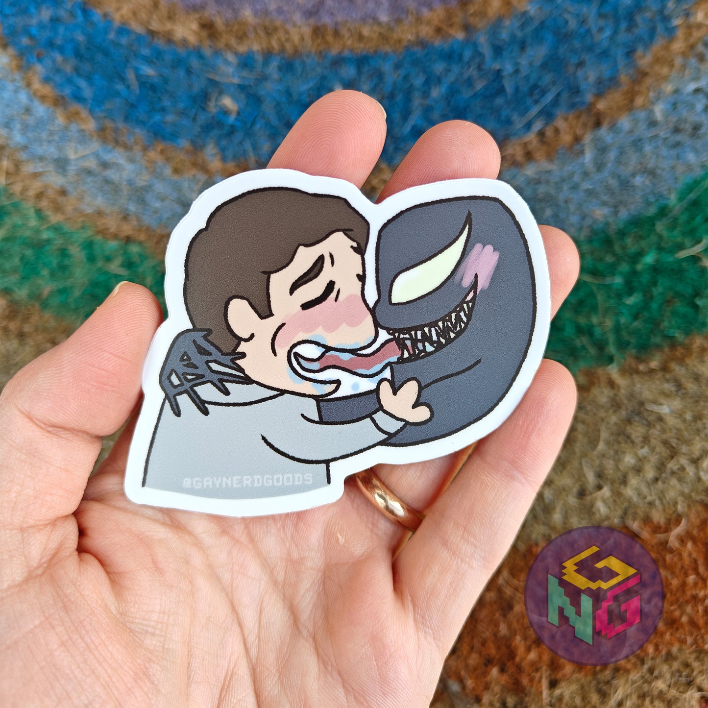 venom and eddie kissing waterproof sticker held in front of a neutral rainbow background