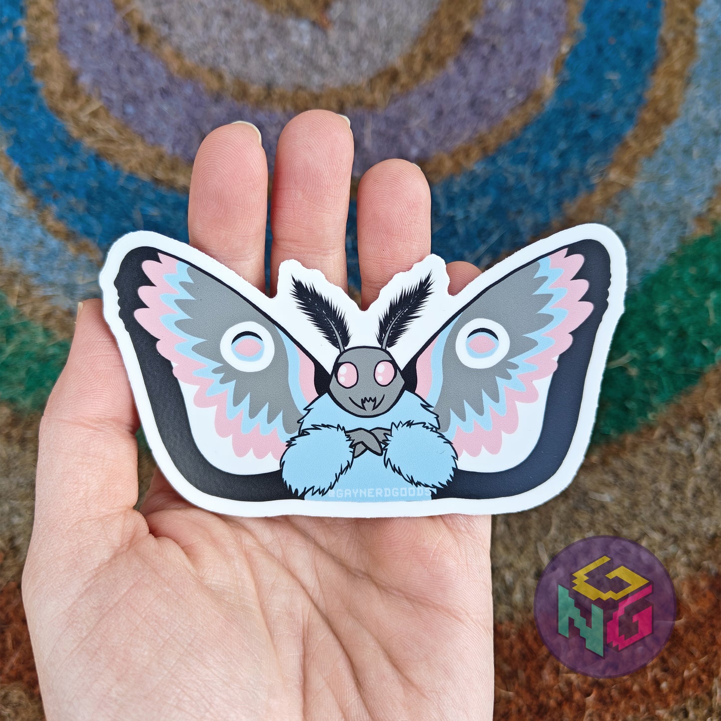 transgender color mothman waterproof sticker held in front of a neutral rainbow background