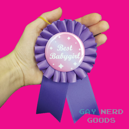 hand holding the best babygirl award ribbon on a pink background