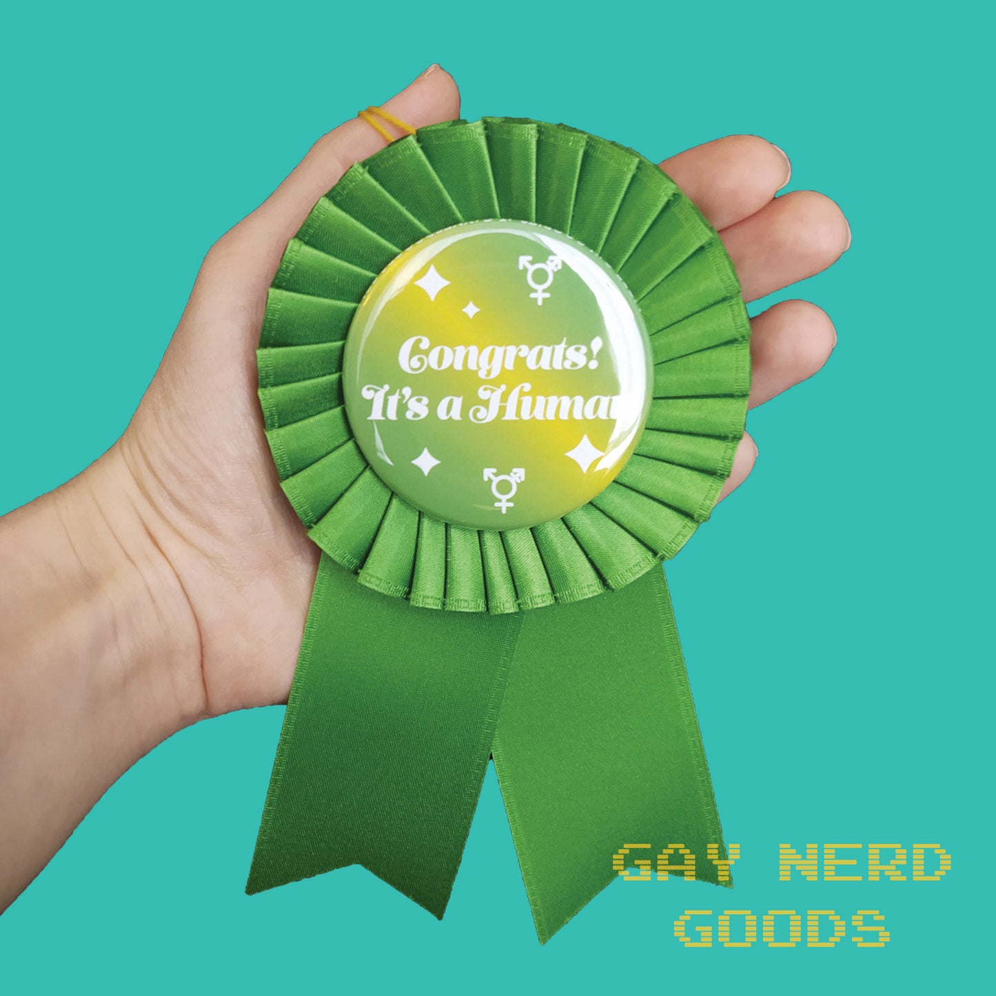 hand holding the green "congrats! it's a human" ribbon rosette on a mint background