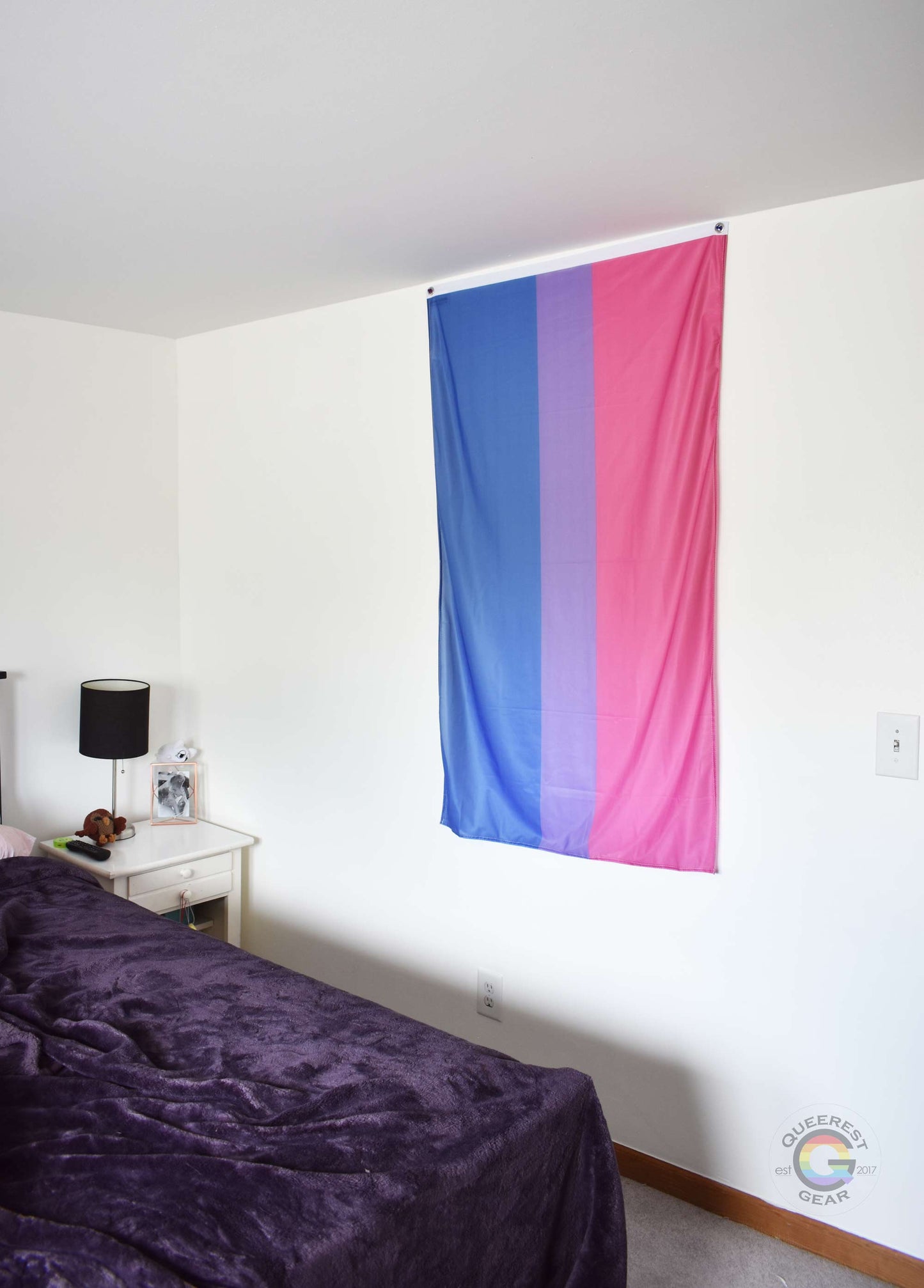 3’x5’ bisexual pride flag hanging vertically on the wall of a bedroom with a nightstand and a bed