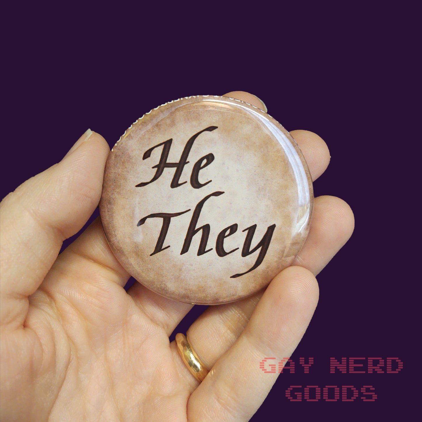 he they large calligraphy pronoun button held in a hand