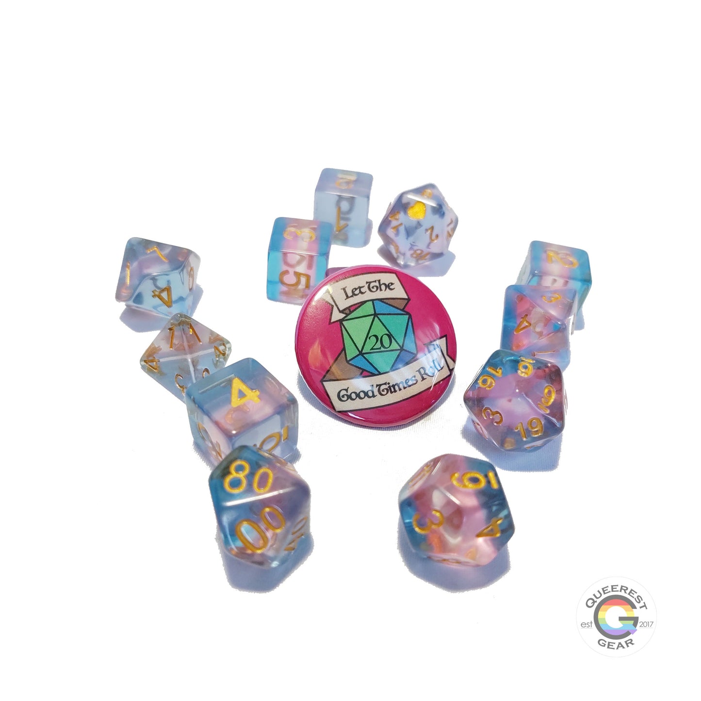 11 piece set of polyhedral dice scattered on a white background. They are transparent and colored in the stripes of the transgender flag with gold ink. There is the freebie “let the good times roll” pinback button among them. 