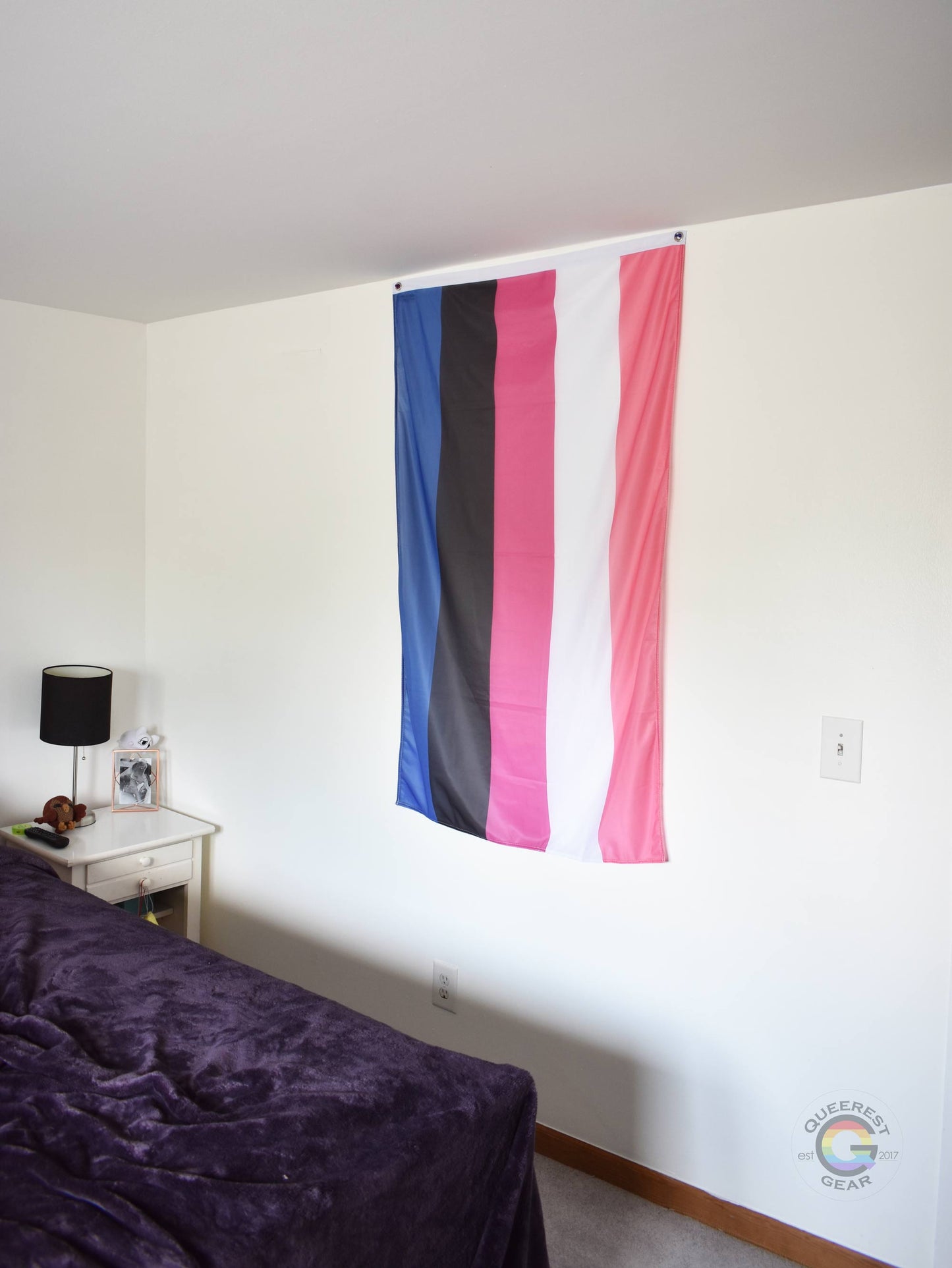 3’x5’ genderfluid flag hanging vertically on the wall of a bedroom with a nightstand and a bed