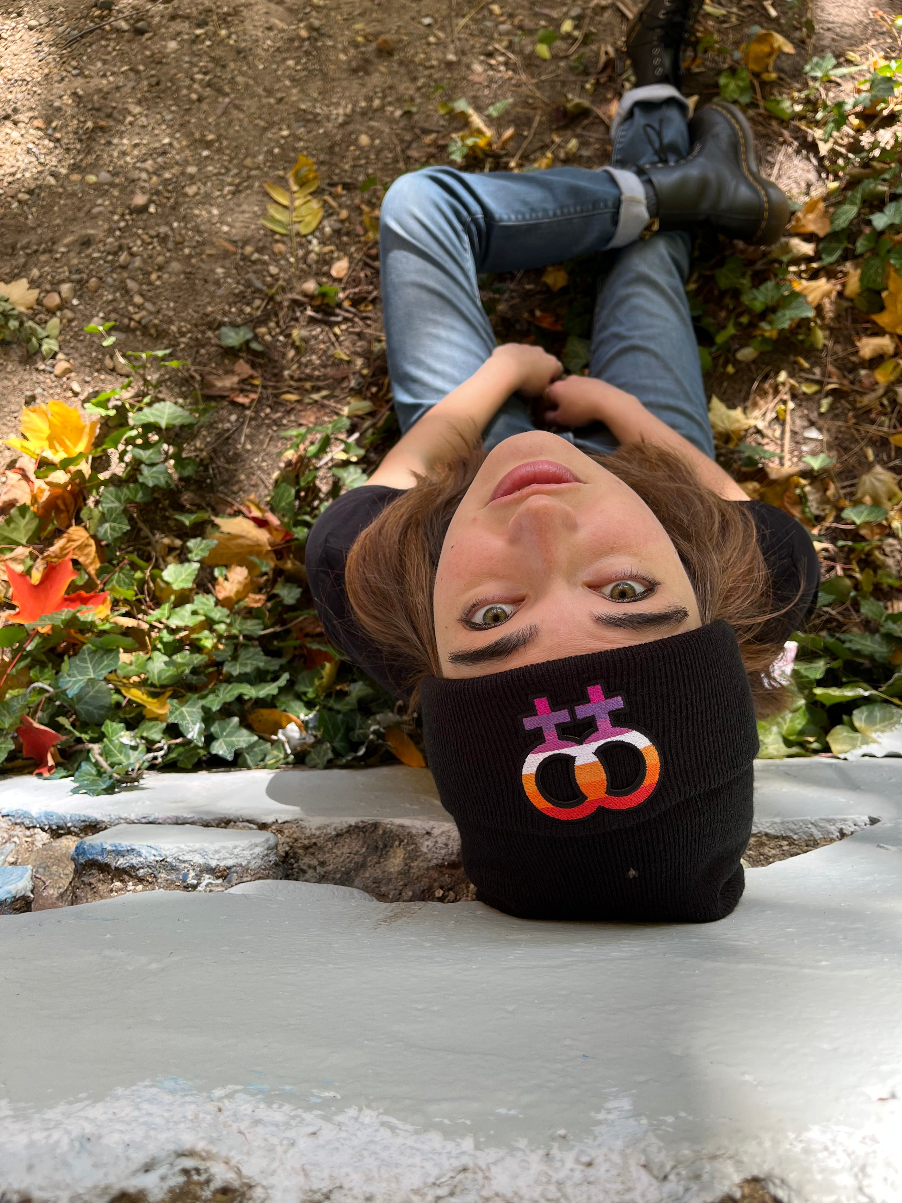 top down view of a person sitting leaning against a wall. they are looking back and up and wearing the lesbian beanie
