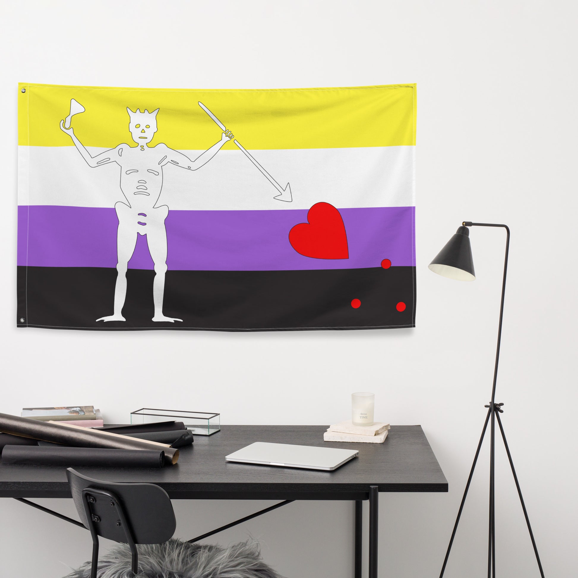 the nonbinary blackbeard pirate flag hanging on a white wall above a small black desk and lamp