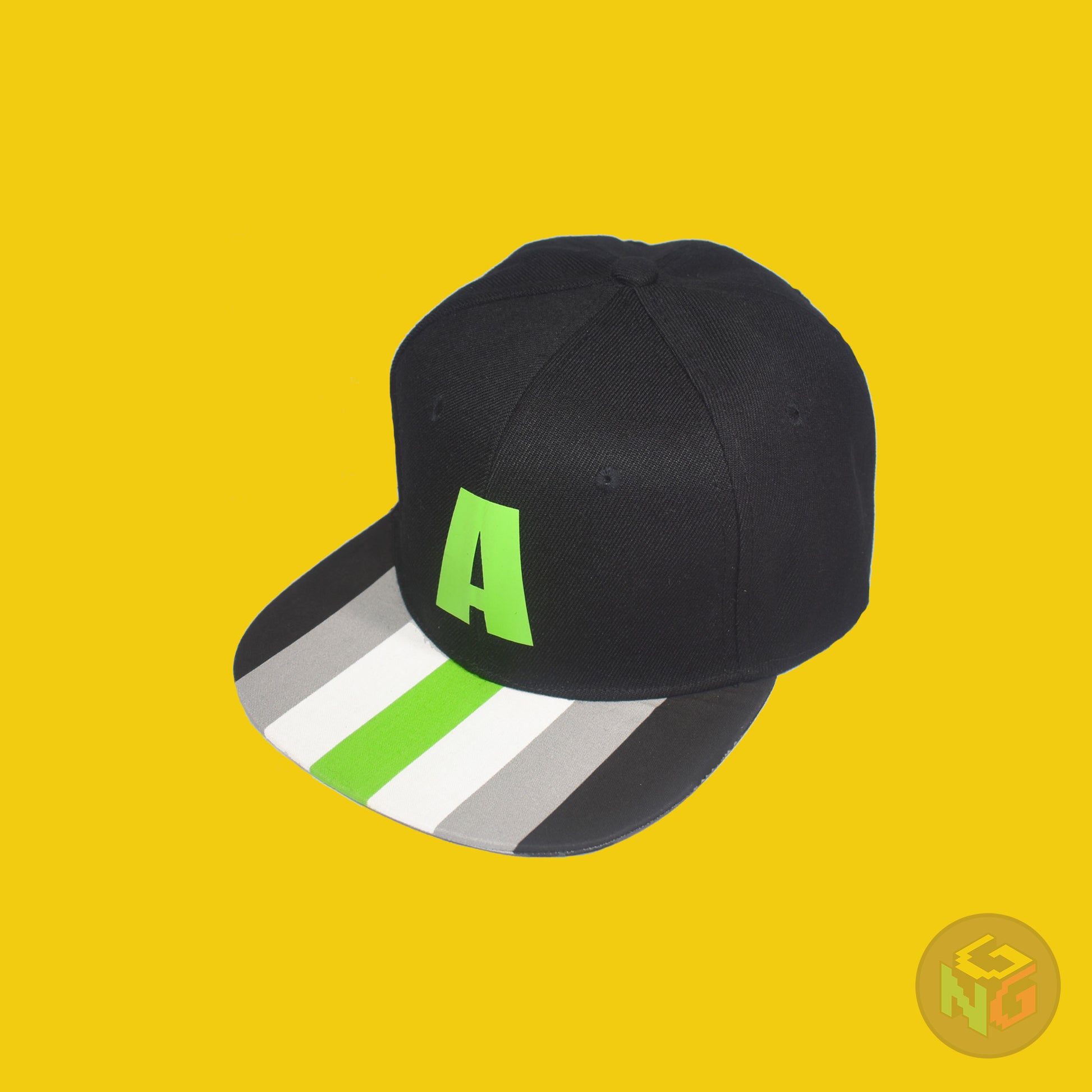 Black flat bill snapback hat. The brim has the agender pride flag on both sides and the front of the hat has a green letter “A”. Front left view