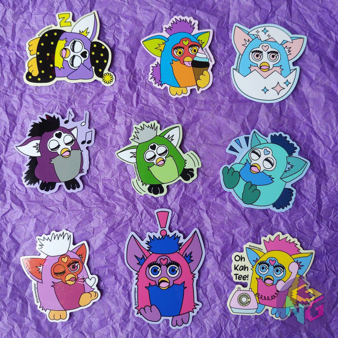 all the pride furby stickers laid out on a purple background. there's a nonbinary, rainbow, transgender, asexual, aromantic, gay, lesbian, bisexual, and pansexual furby