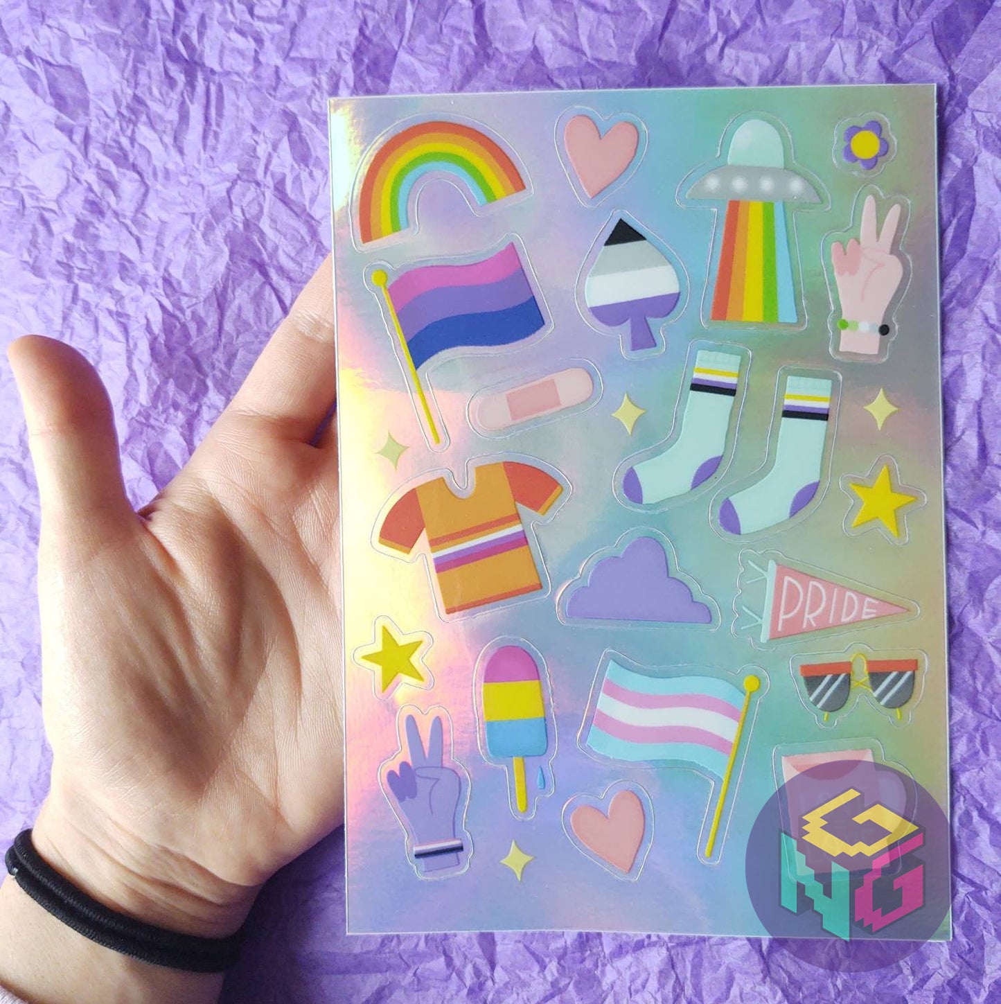 andyrogyny and gay nerd goods rainbow holographic sticker sheet with over twenty tiny pride stickers held by a hand on purple background
