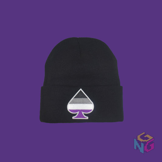 Black knit fabric beanie with the asexual ace of spades symbol in asexual black, white, grey, and purple on the front. It is laying flat on a purple background