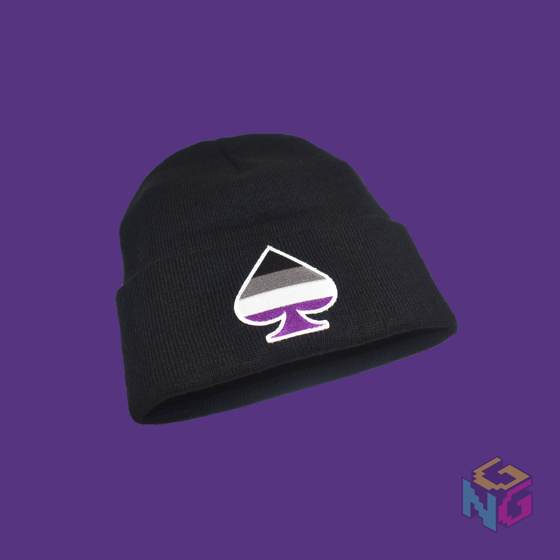 Black knit fabric beanie with the asexual ace of spades symbol in asexual black, white, grey, and purple on the front. It's lying at an angle on a purple background