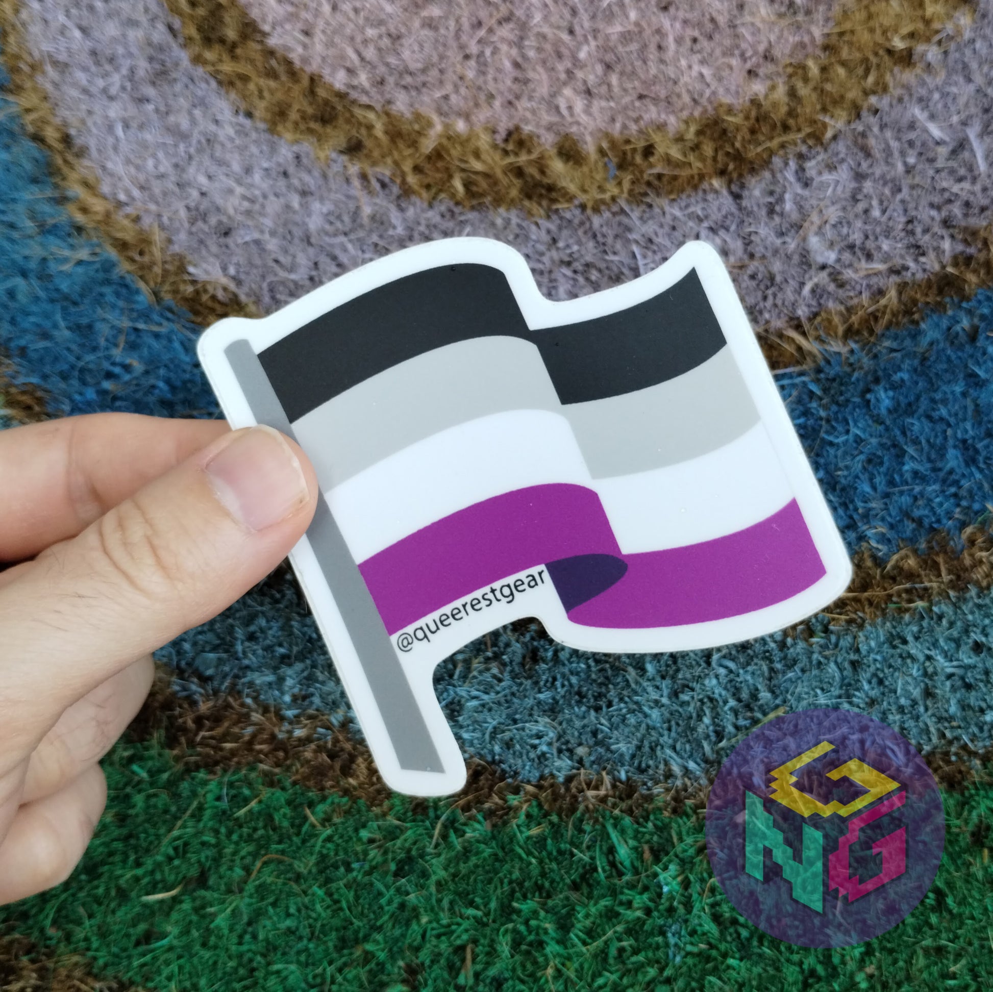 asexual flag sticker held in thumb and finger on rainbow welcome mat