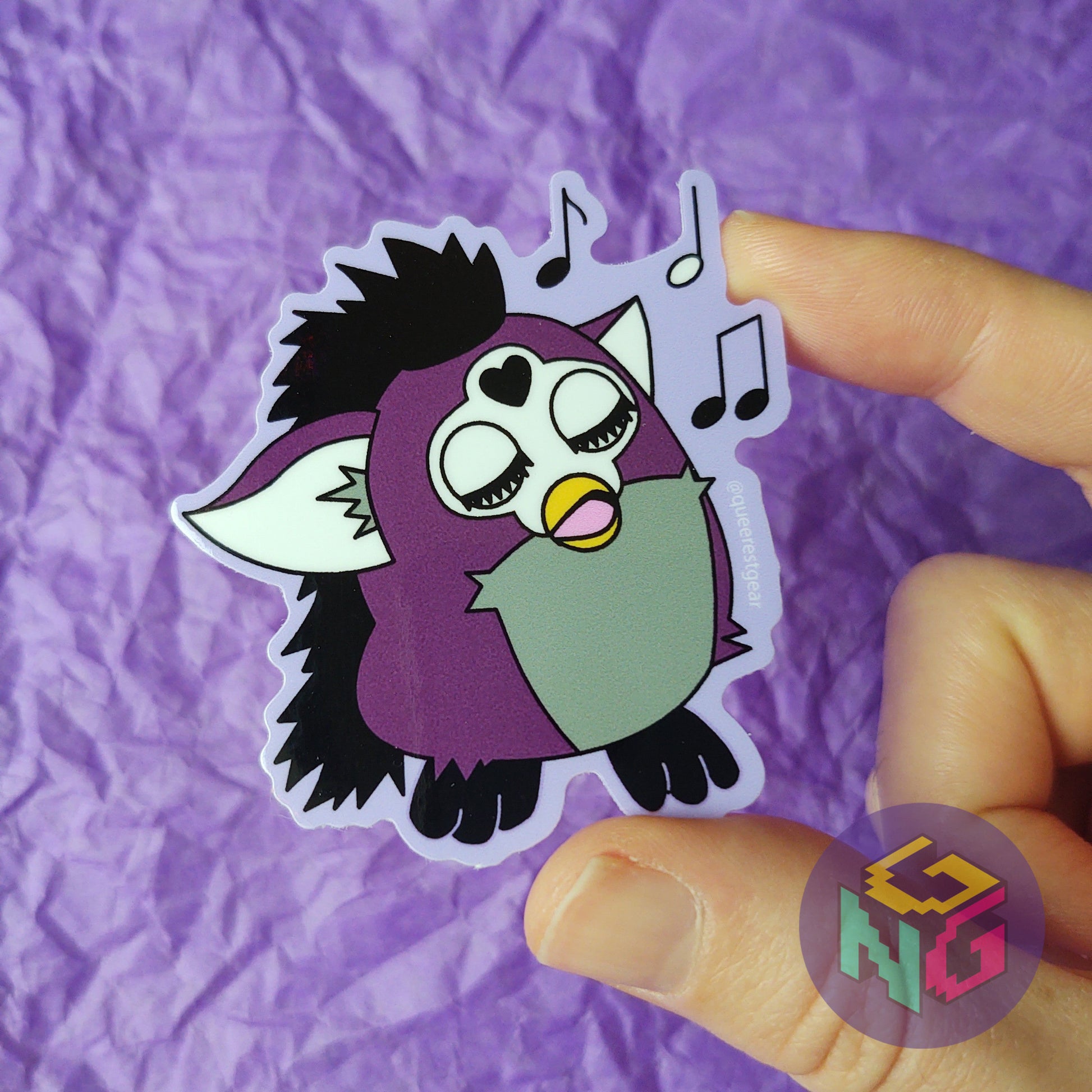 asexual singing furby sticker held in a hand in front of a purple background