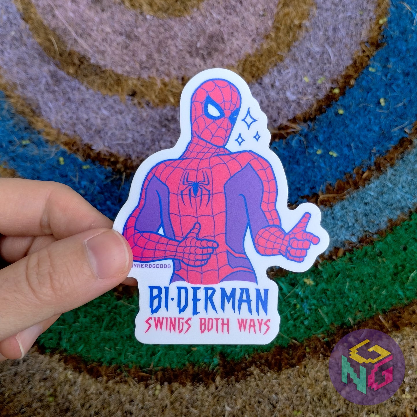 biderman matte sticker held in a hand in front of a rainbow welcome mat