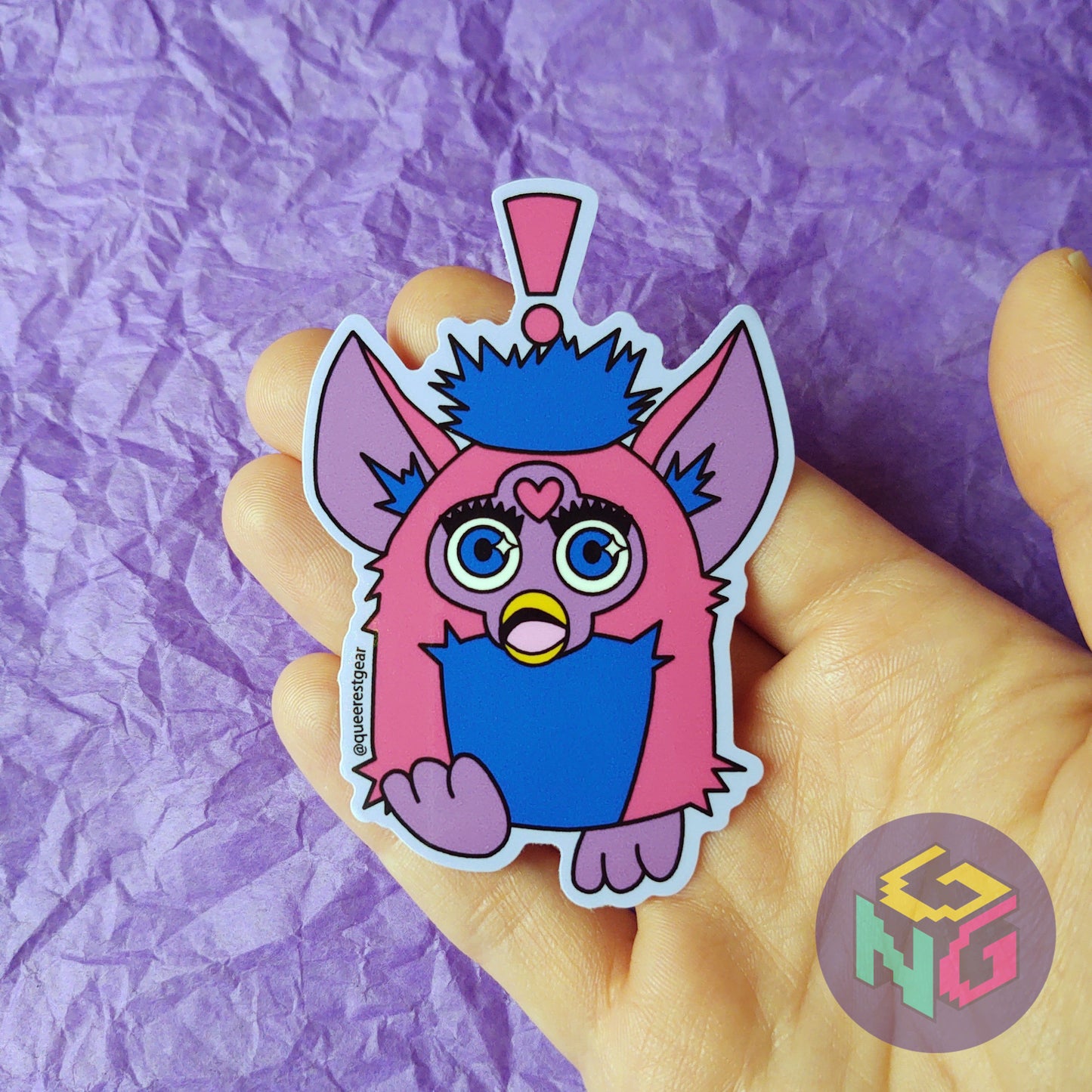 bisexual surprised furby sticker held in a hand in front of a purple background