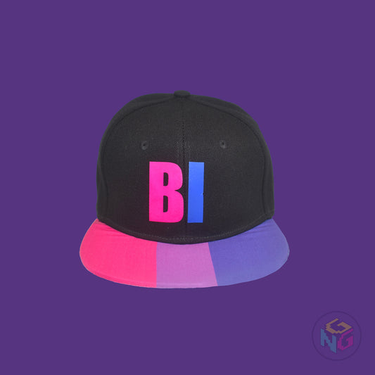 Black flat bill snapback hat. The brim has the bisexual pride flag on both sides and the front of the hat has the word “BI” in pink and blue. Front view