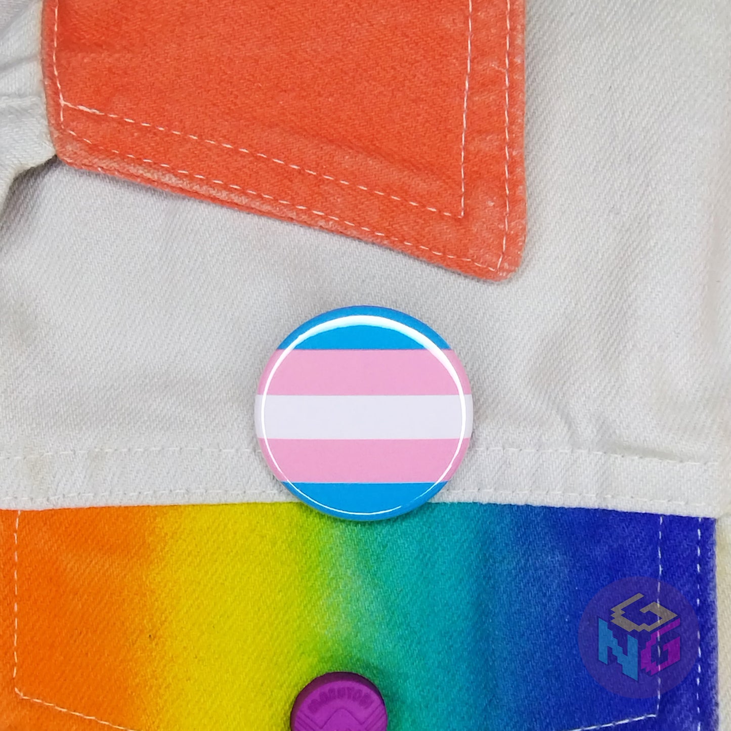 round transgender flag pin attached to a white and rainbow denim jacket