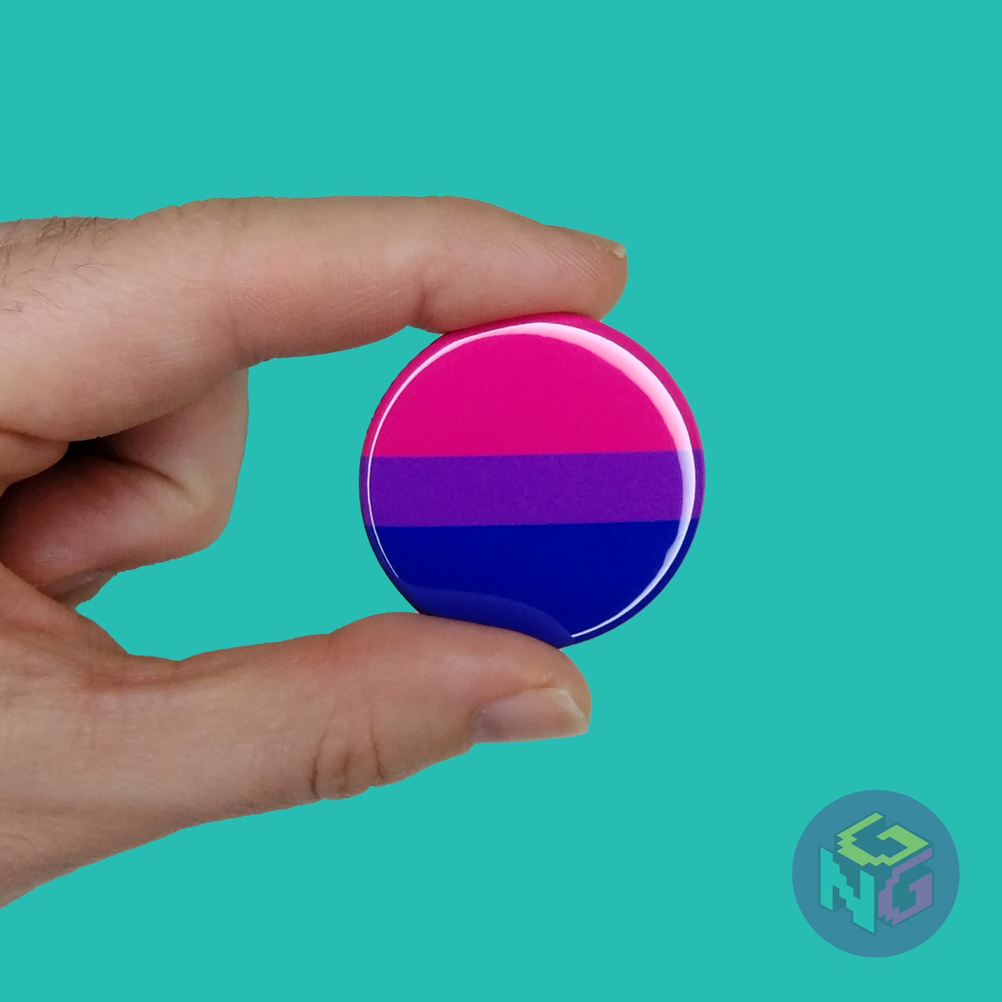 round bisexual pride pin being held by a hand in front of a mint background