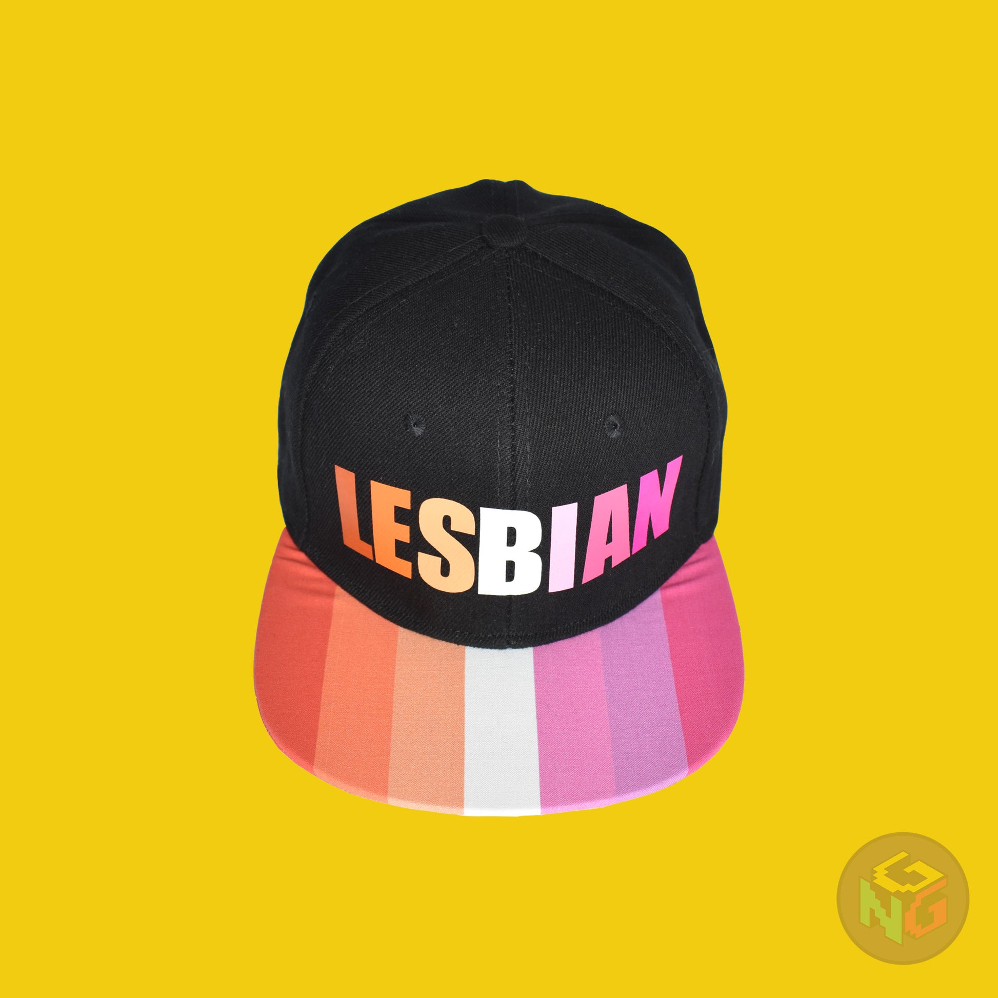 Black flat bill snapback hat. The brim has the lesbian pride flag on both sides and the front of the hat has the word “LESBIAN” in orange, pink, and white letters. Front top view