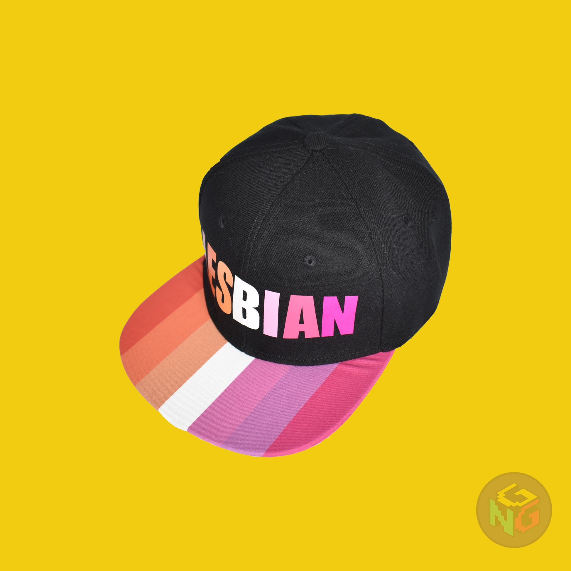 Black flat bill snapback hat. The brim has the lesbian pride flag on both sides and the front of the hat has the word “LESBIAN” in orange, pink, and white letters. Front left view