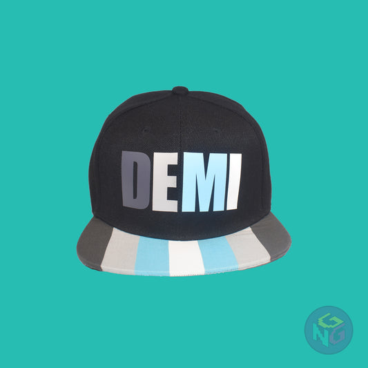 Black flat bill snapback hat. The brim has the demiboy pride flag on both sides and the front of the hat has the word “DEMI” in dark grey, light grey, blue, and white. Front view