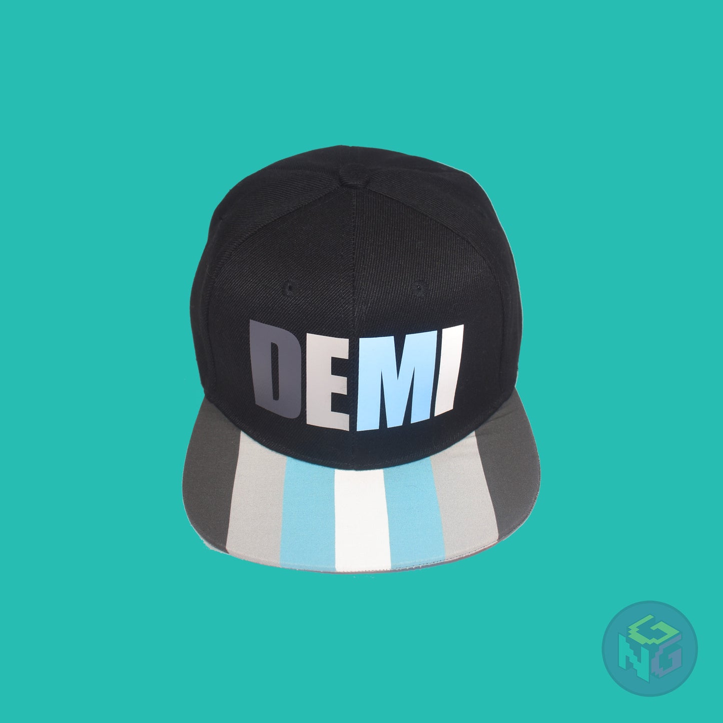 Black flat bill snapback hat. The brim has the demiboy pride flag on both sides and the front of the hat has the word “DEMI” in dark grey, light grey, blue, and white. Front top view
