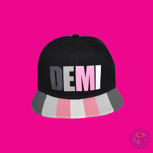 Black flat bill snapback hat. The brim has the demigirl pride flag on both sides and the front of the hat has the word “DEMI” in dark grey, light grey, pink, and white. Front view