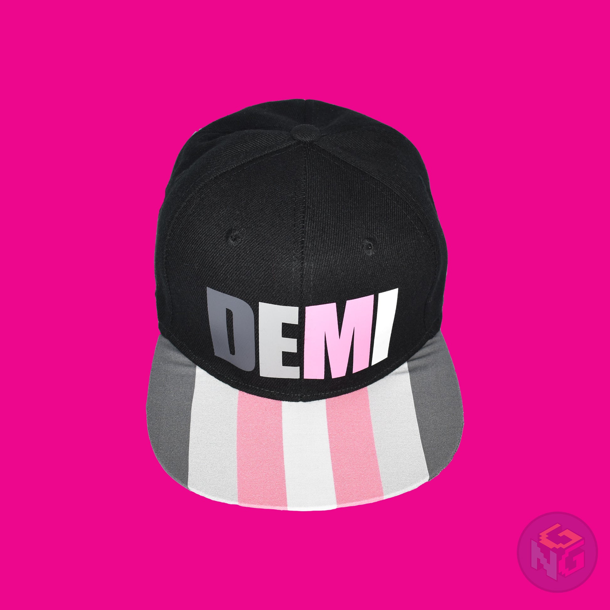 Black flat bill snapback hat. The brim has the demigirl pride flag on both sides and the front of the hat has the word “DEMI” in dark grey, light grey, pink, and white. Front top view