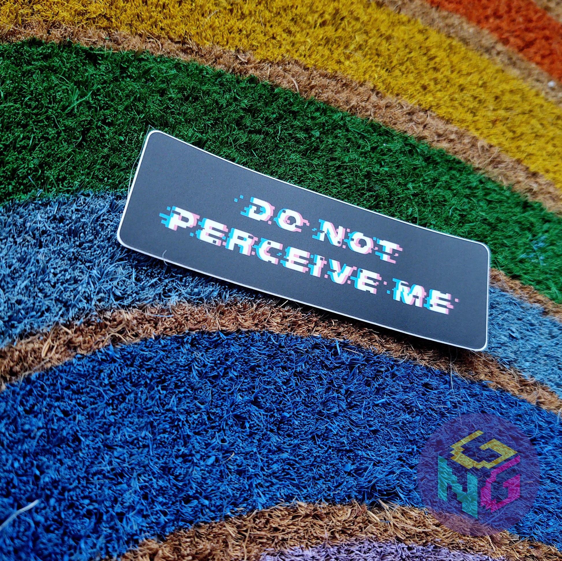 do not perceive me sticker lying at an angle on a rainbow welcome mat