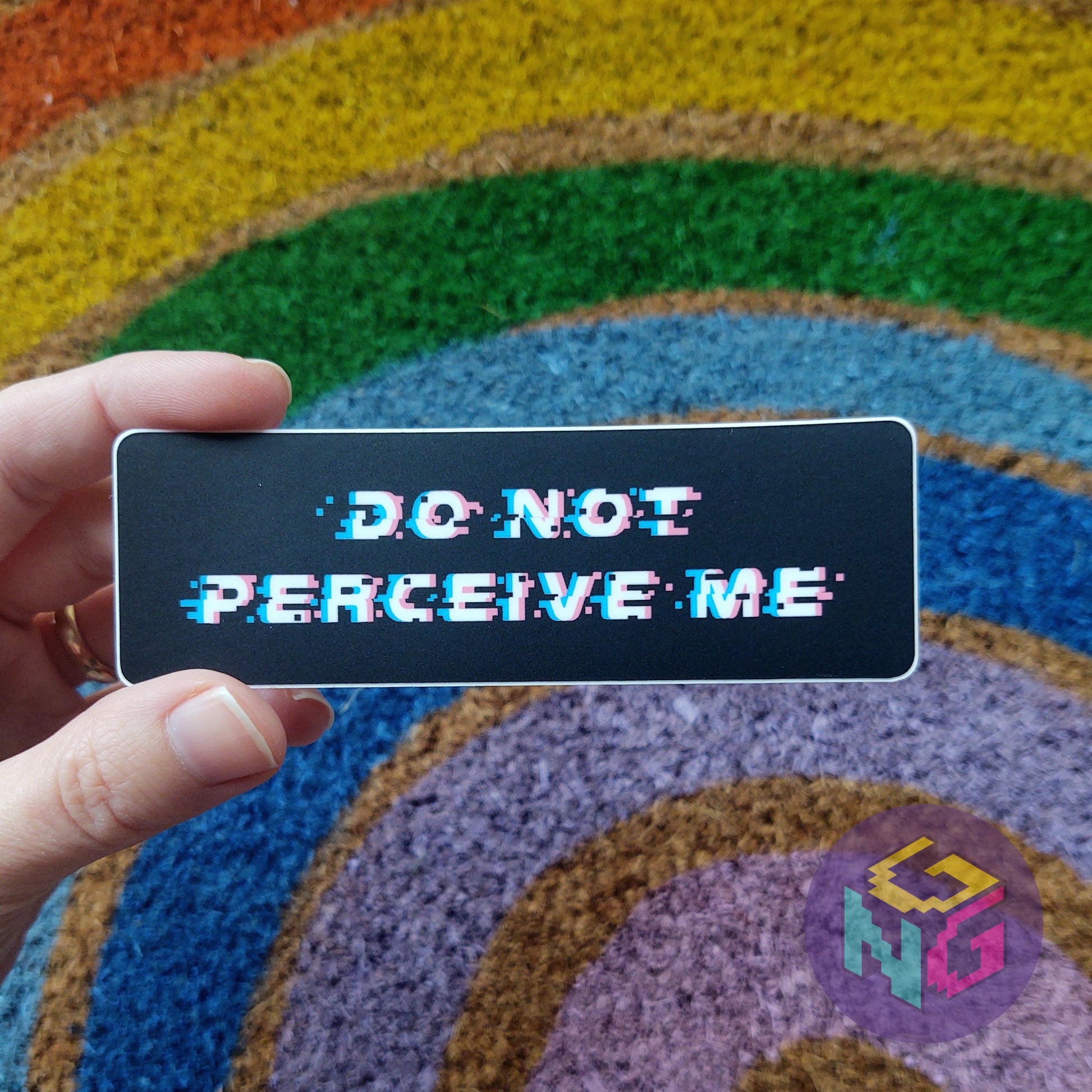 do not perceive me sticker held in front of a rainbow welcome mat