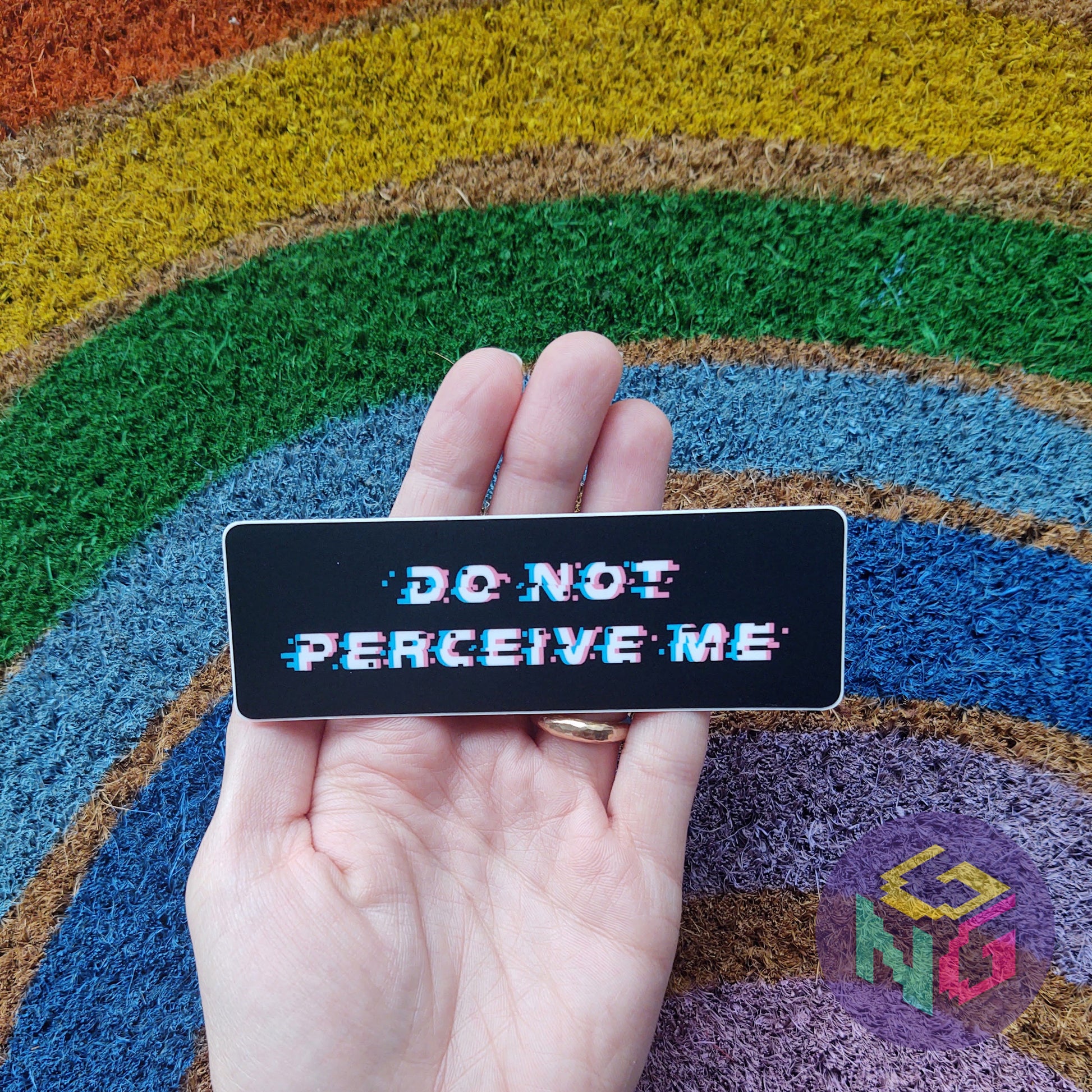 do not perceive me sticker held in a hand in front of rainbow welcome mat