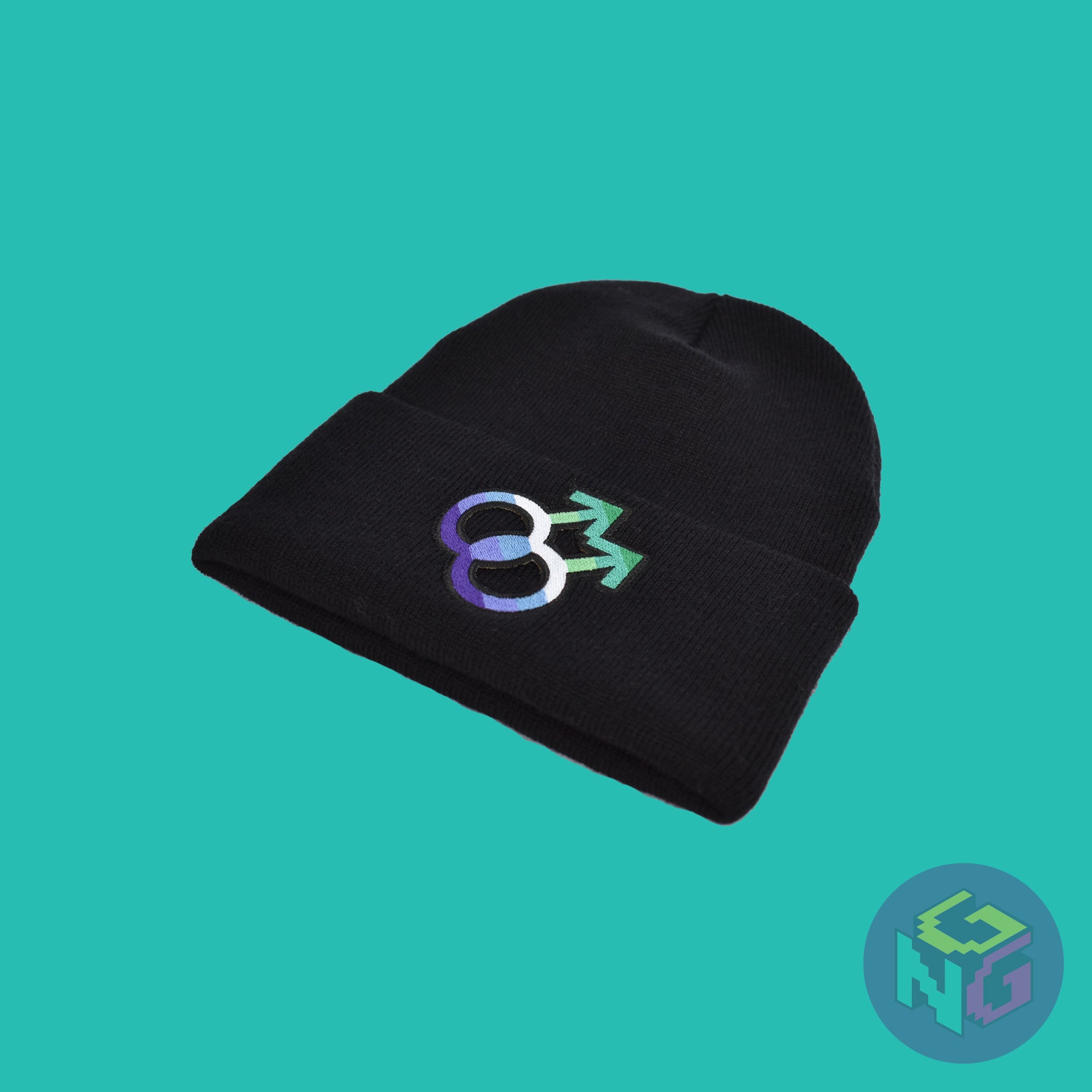 Black knit fabric beanie with the gay symbol in greens, blues, and white on the front. It is laying flat seen from a lower right view