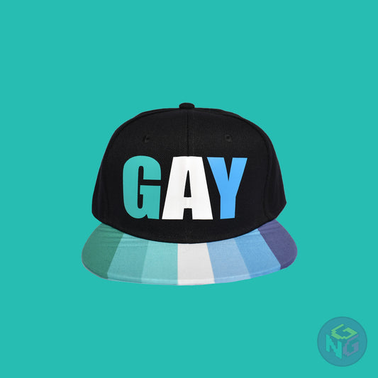 Black flat bill snapback hat. The brim has the gay pride flag on both sides and the front of the hat has the word “GAY” in turquoises, blues, and white. Front view