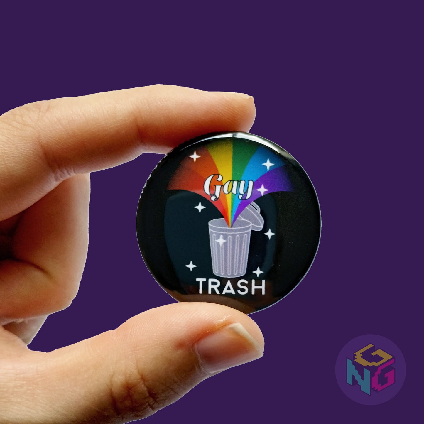 gay trash button held in hand in front of dark purple background