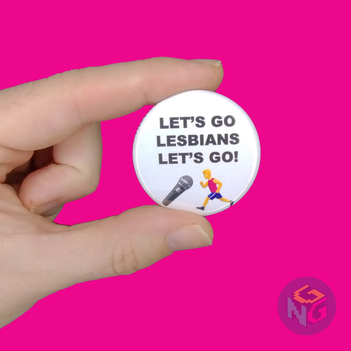 light skin hand holding the round white let's go lesbians pin in front of a pink background