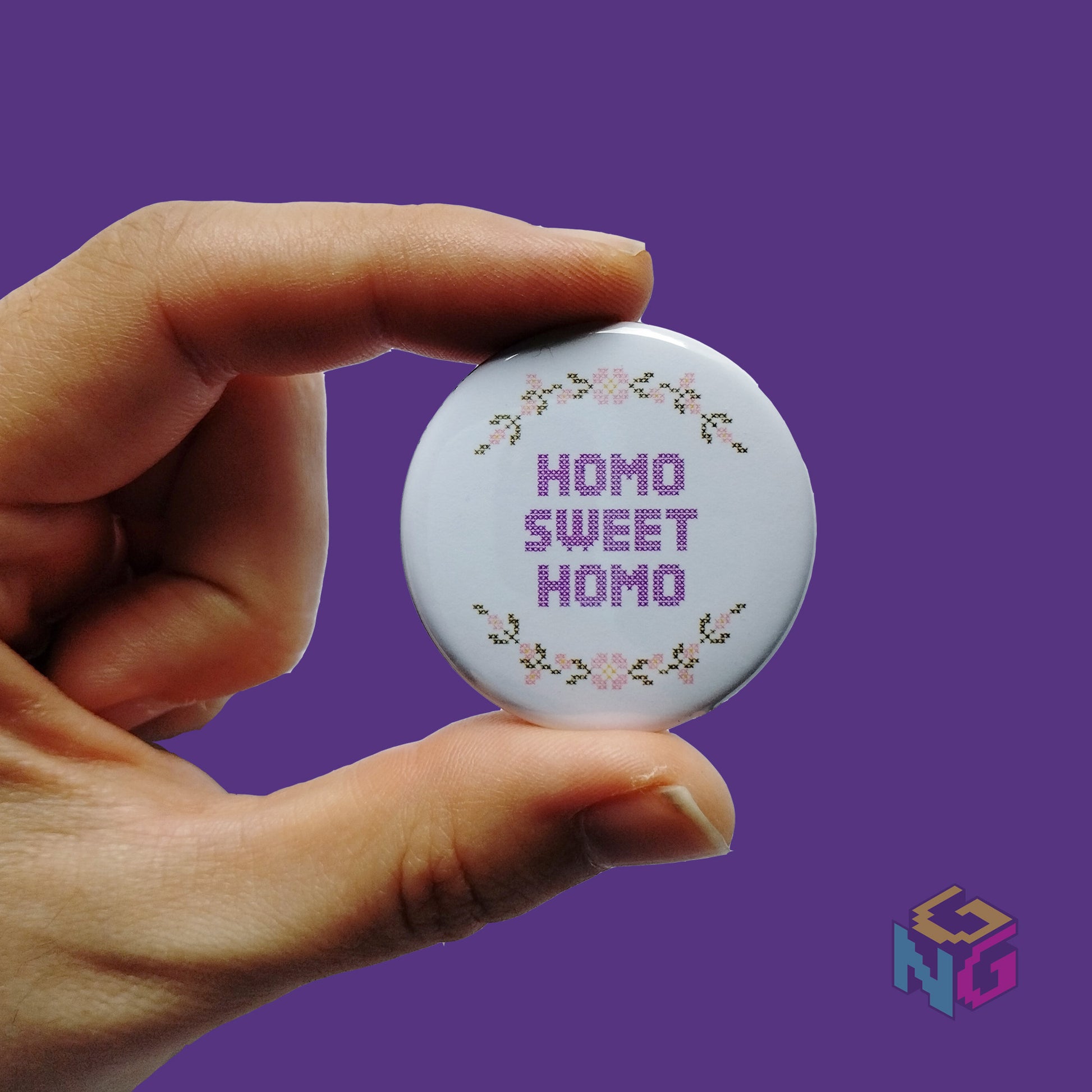 round homo sweet homo button held in hand in front of purple background