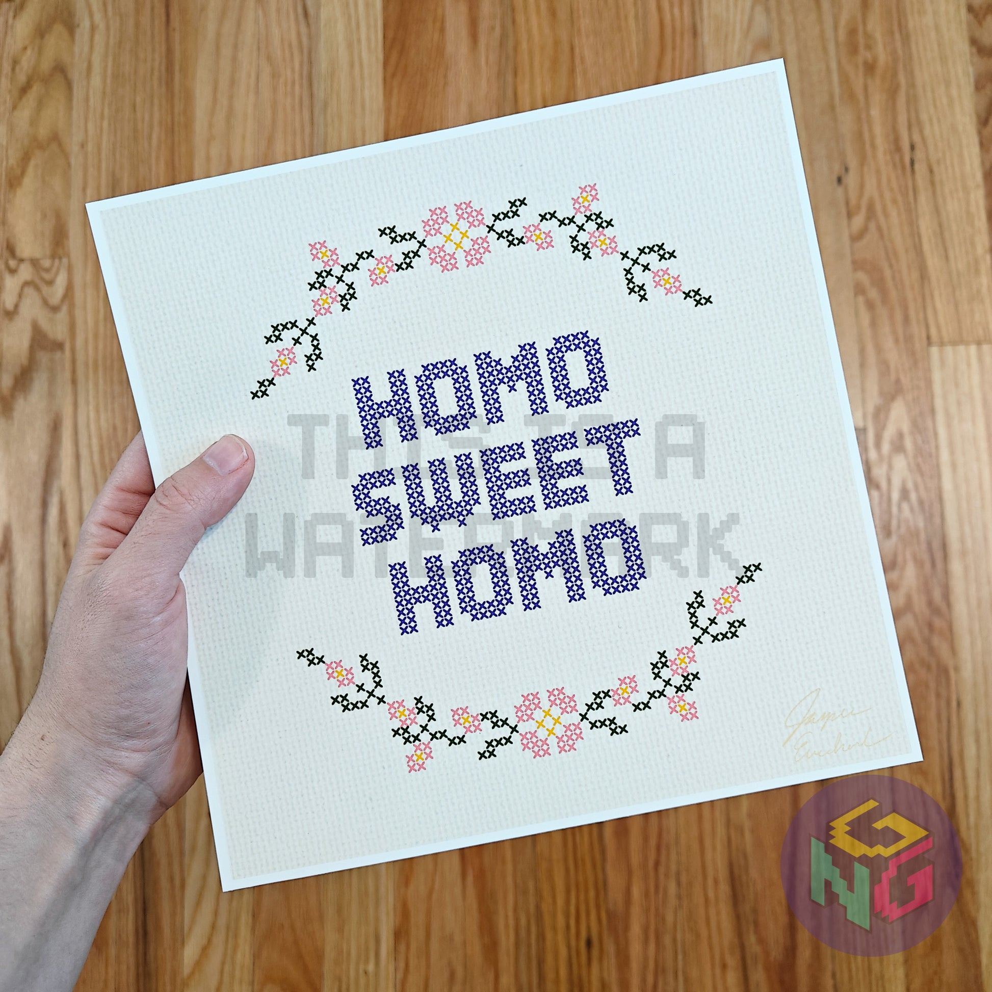 art print in an embroidery style showing a circle of flowers and the text "homo sweet homo" against a wood background