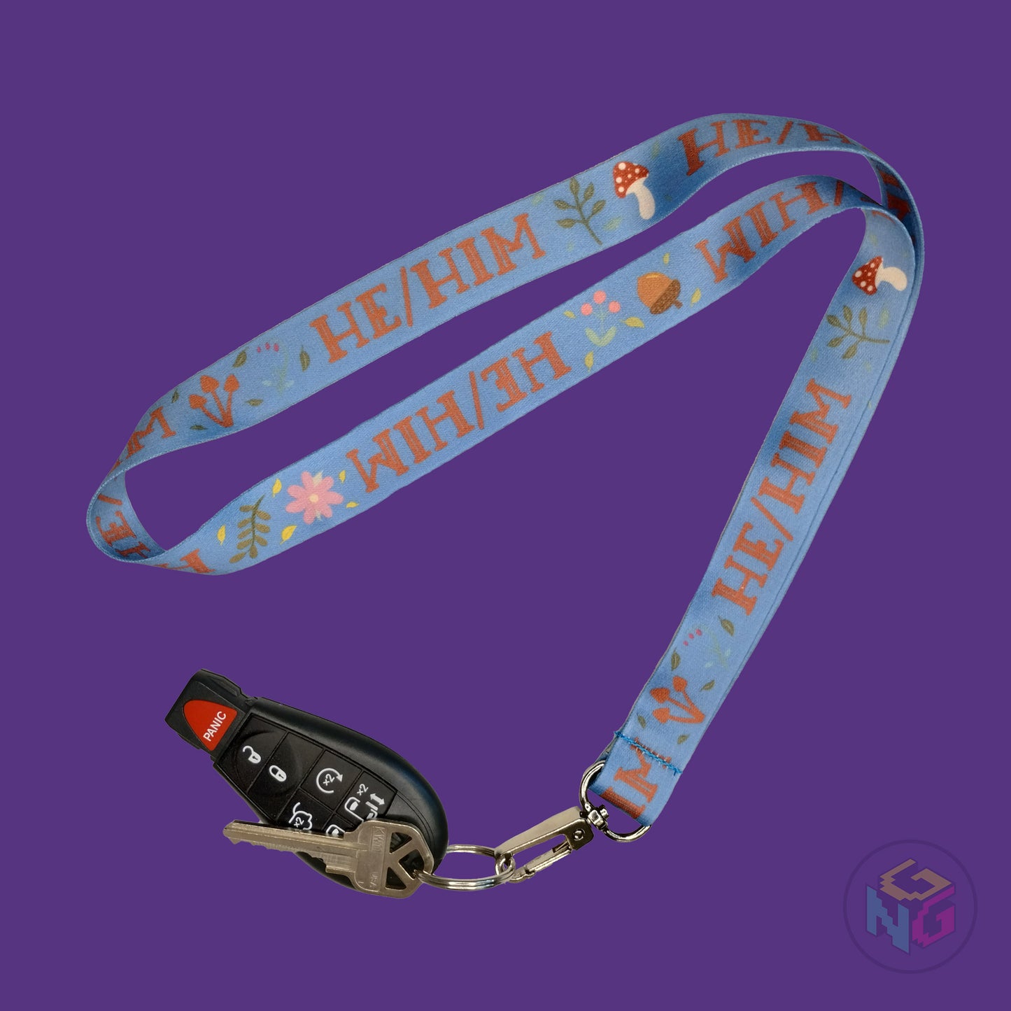 blue he him pronoun lanyard showing the brown text, mushrooms, leaves, and flower details with a key fob clipped to the end of the lanyard