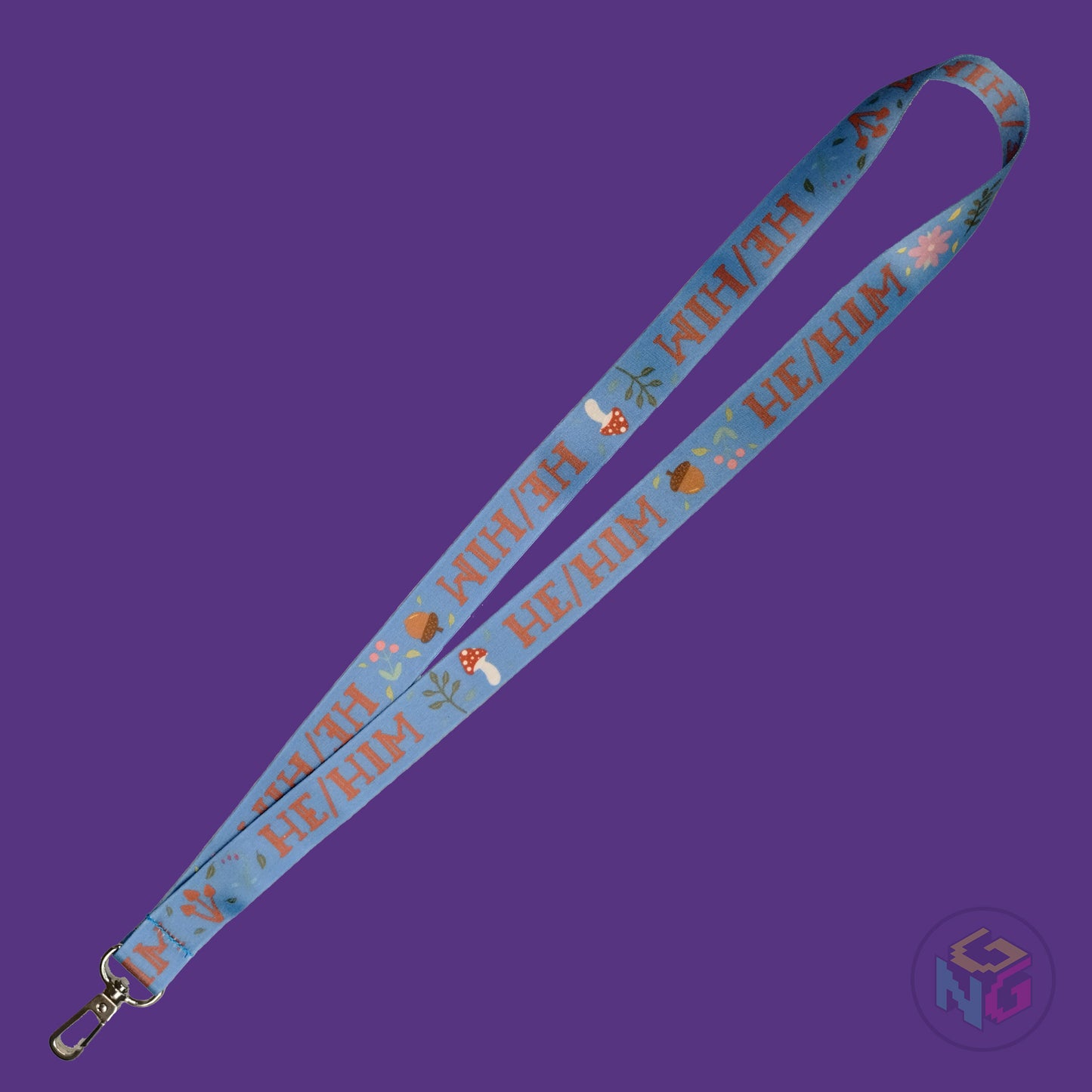 the blue he him cottagecore lanyard lying flat showing the complete design and repeating pattern of acorns, berries, mushrooms, leaves, and he him pronouns.