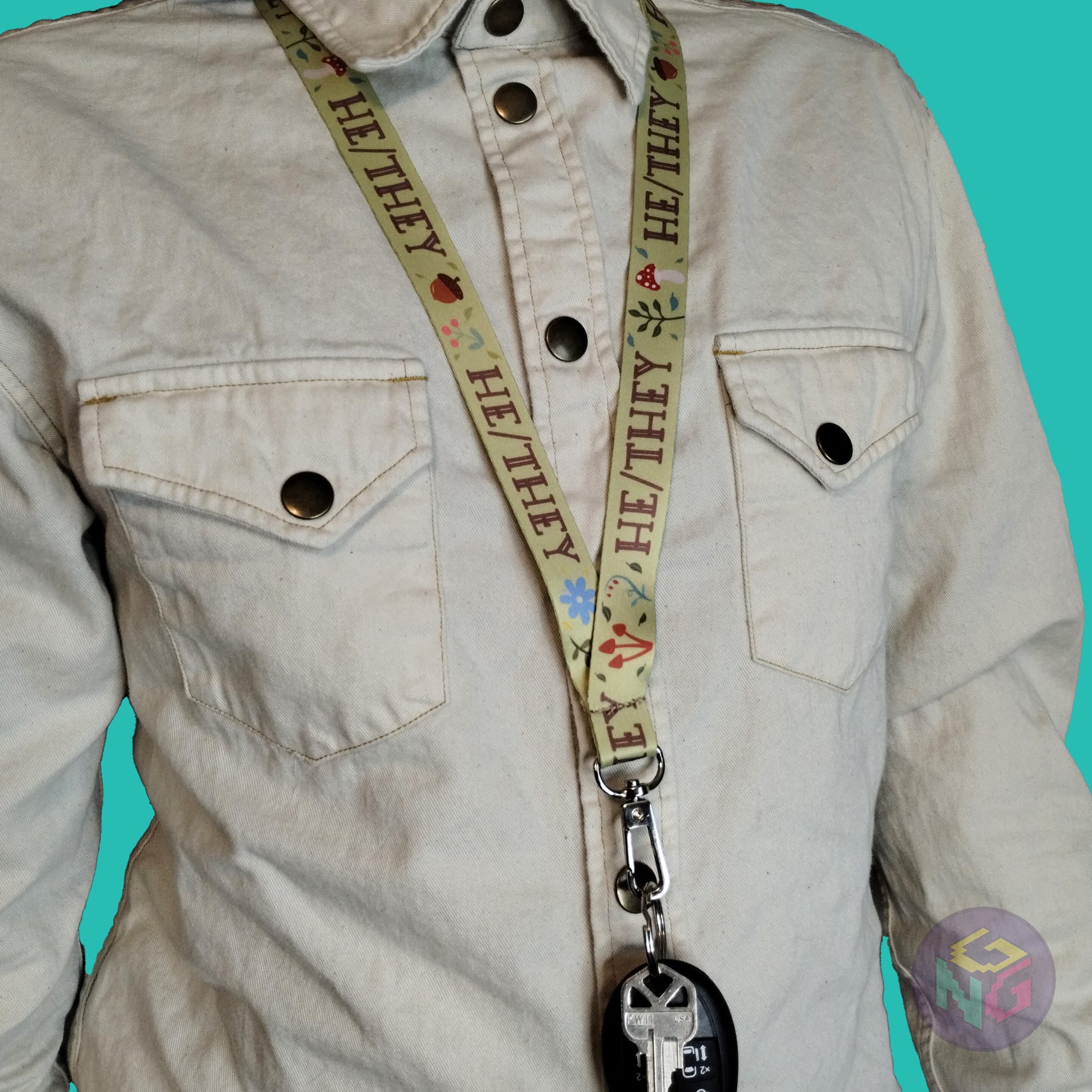 green he they mushroom lanyard being worn by a flat chested person wearing a cream button up. The end of the lanyard falls between their sternum and bellybutton and has a key fob clipped to the end